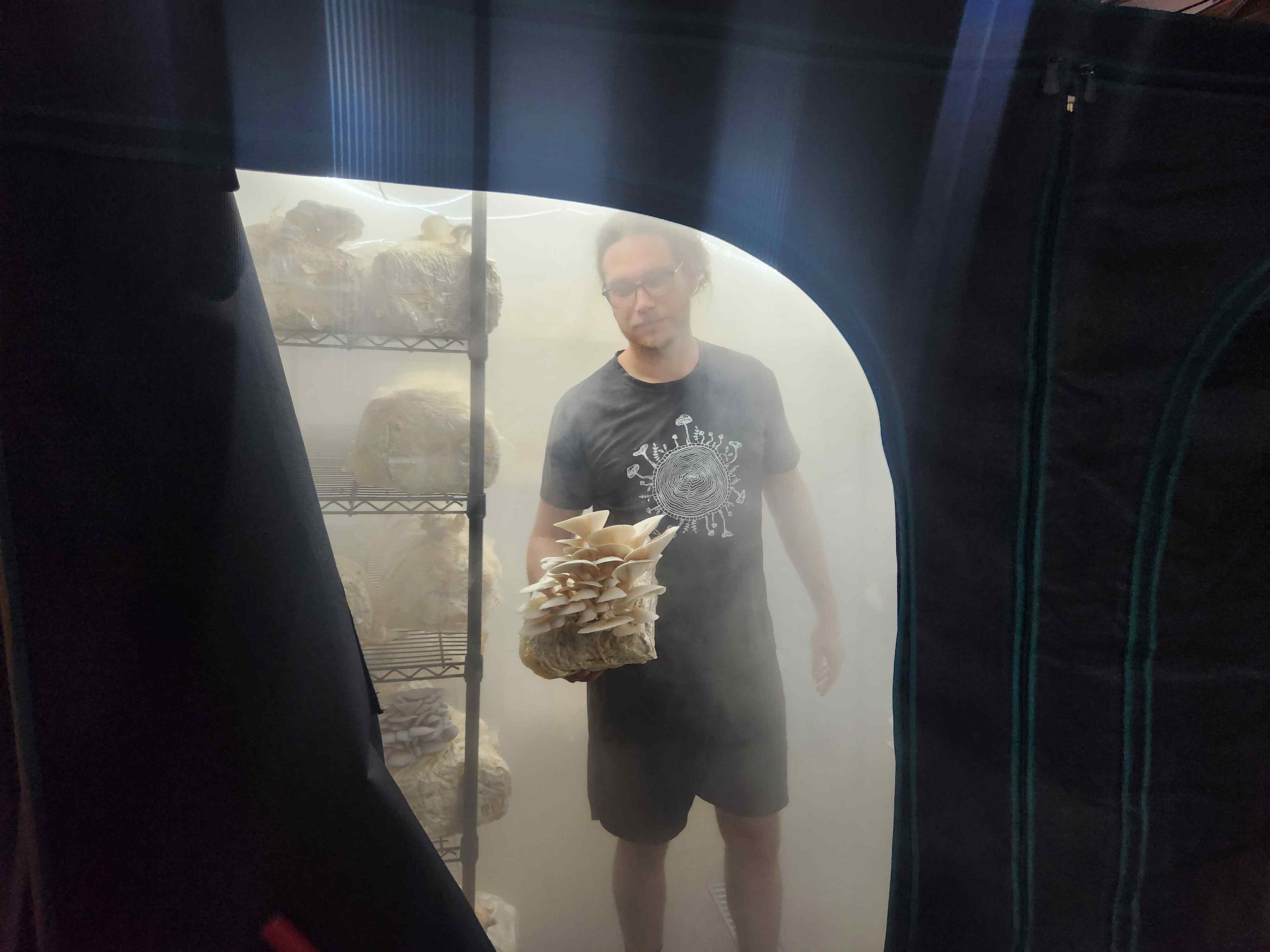 Shane in a mushroom tent holding mushrooms